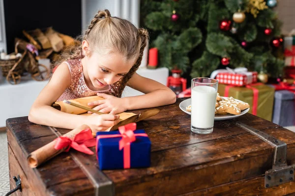 Mignon souriant enfant écriture wishlist sur parchemin à noël temps — Photo de stock