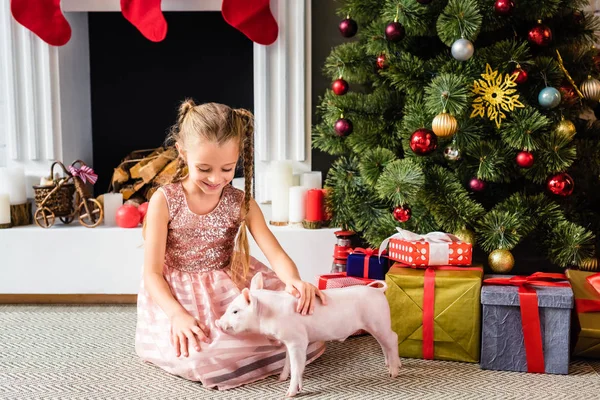 Entzückend lächelndes Kind, das zur Weihnachtszeit mit Ferkeln spielt — Stockfoto