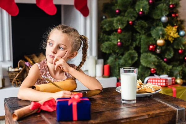 Cute pensive kid writing wishlist on parchment at christmas time — Stock Photo