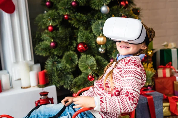 Cute smiling child sitting in sled and using virtual reality headset at christmas time — Stock Photo