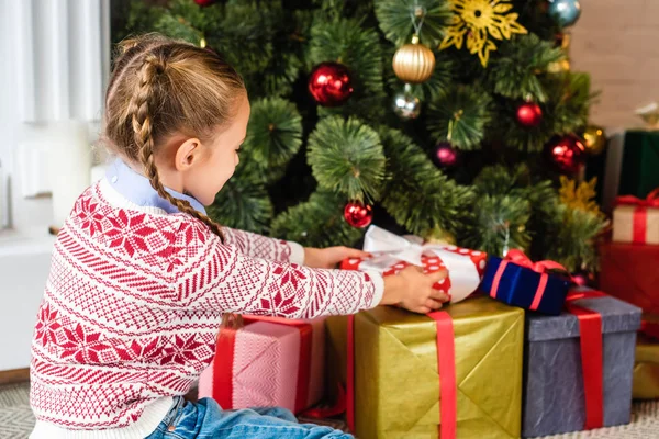 Side view of cute kid opening gift boxes under christmas tree — Stock Photo