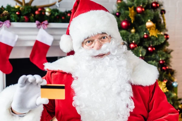 Santa claus celebración de la tarjeta de crédito y mirando a la cámara - foto de stock