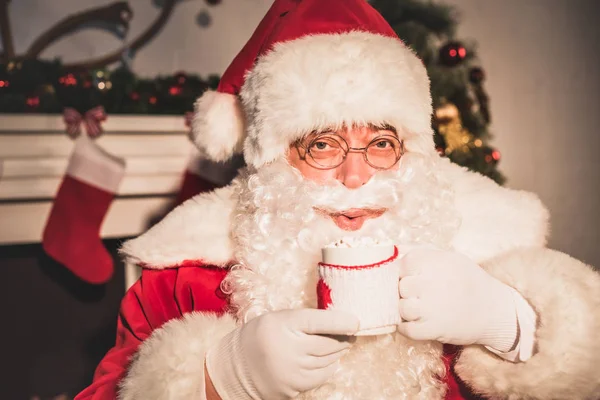 Санта п'є гарячий напій з зефіром і дивиться на камеру — стокове фото