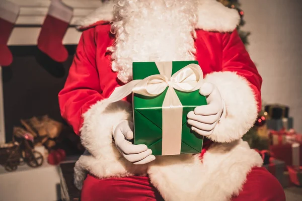 Plan recadré de Père Noël tenant cadeau de Noël tout en étant assis près de la cheminée — Photo de stock
