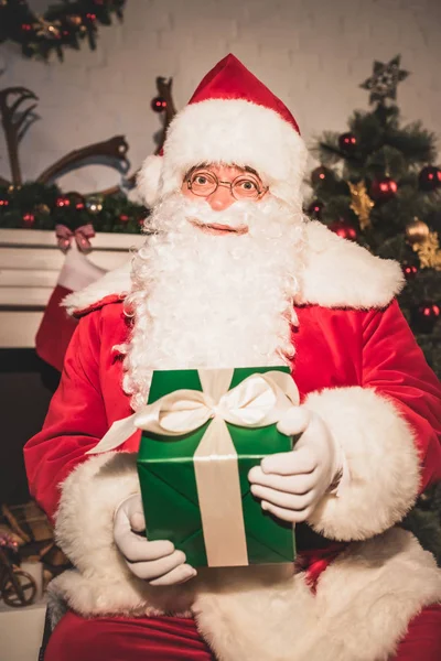Santa Claus tenant cadeau de Noël et regardant la caméra — Photo de stock