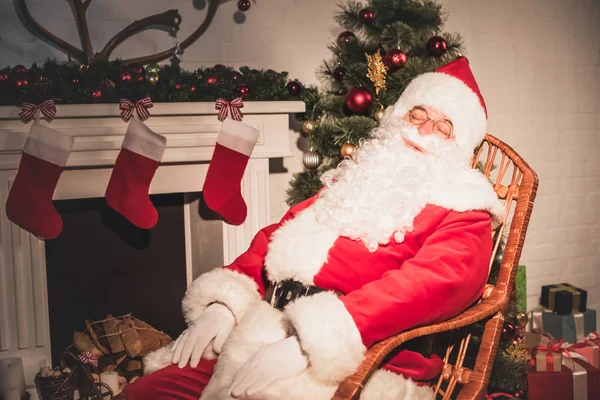 Санта Клаус спить у кріслі біля каміна з шкарпетками — стокове фото