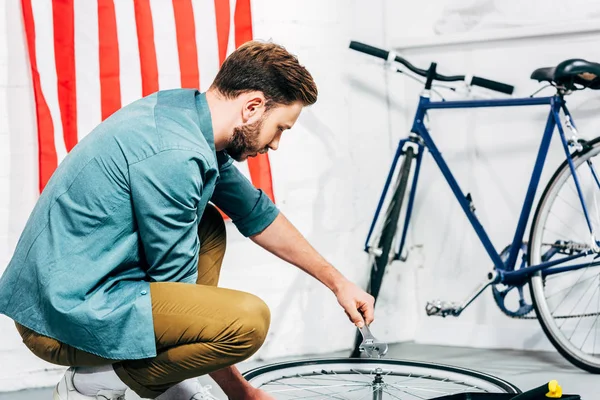 Konzentrierter Reparateur mit verstellbarem Schraubenschlüssel in der Hand, der das Fahrrad fixiert — Stockfoto