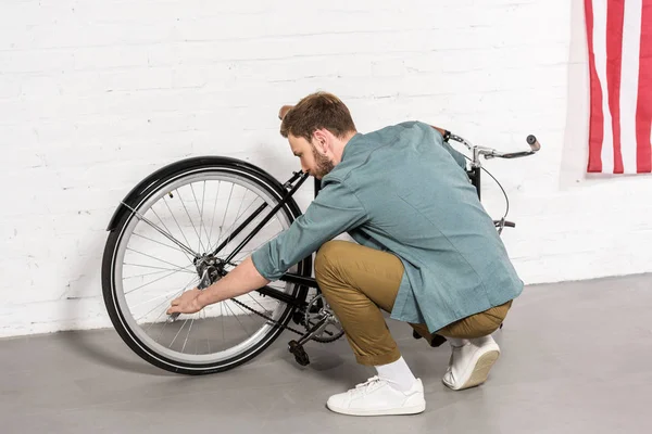 Vue latérale du jeune homme réparant le vélo par clé réglable — Photo de stock