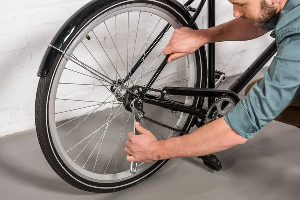 Partial view of young man repairing bicycle by adjustable spanner — Stock Photo