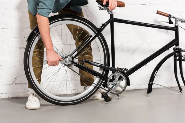 Cropped image of young man repairing bicycle by adjustable spanner — Stock Photo