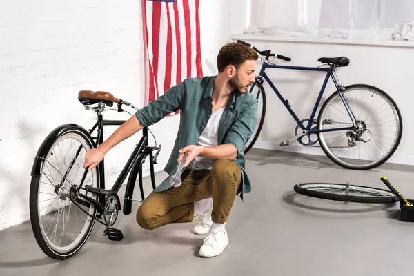 Selective focus of young repairman fixing bicycle by adjustable wrench — Stock Photo