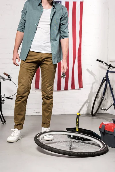 Partial view of man holding wrench in hand near bicycle wheel — Stock Photo