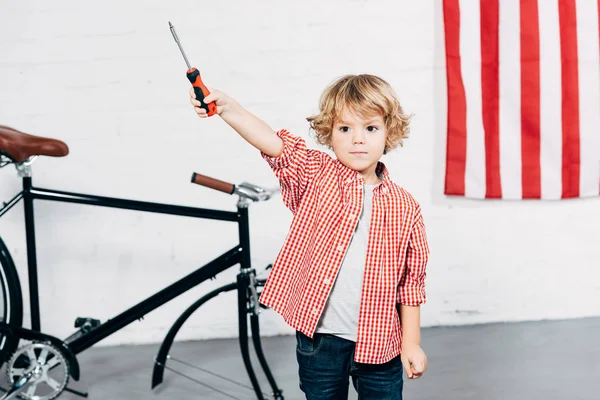 Kid holding screwdriver near disassembled bicycle at workshop — Stock Photo