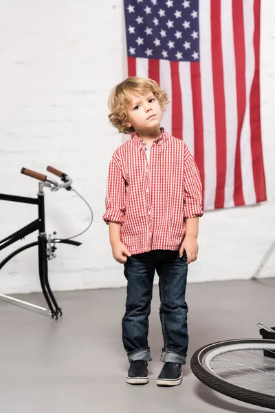 Adorable niño mirando la cámara cerca de la bicicleta desmontada en el taller — Stock Photo