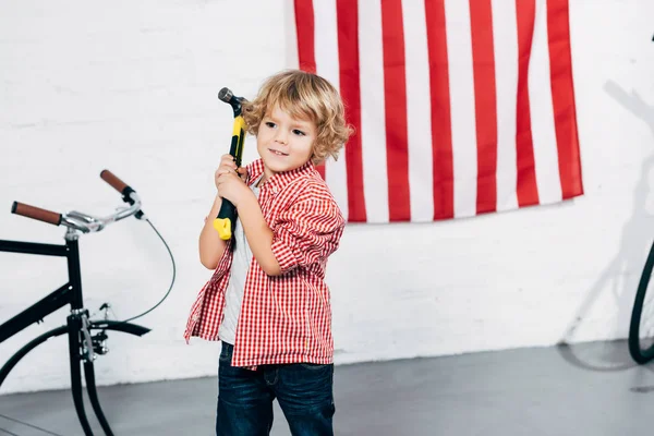 Cheerful curly boy holding hammer near disassembled bicycle — Stock Photo