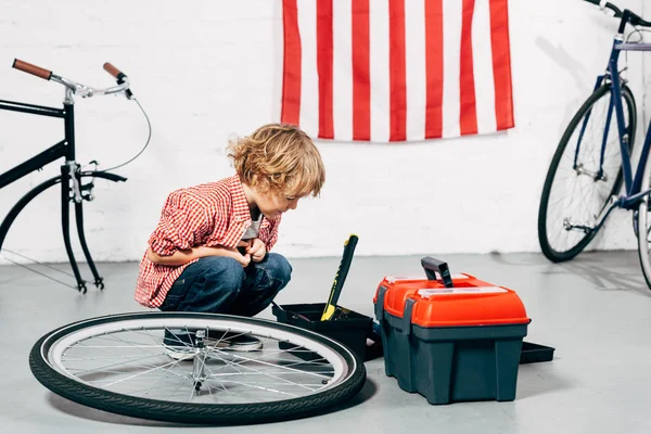 Enfant assis près des boîtes à outils près de la roue de vélo démontée à l'atelier — Photo de stock