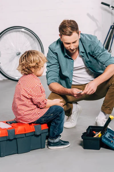 Homem alegre mostrando chave para o filho pequeno na oficina de bicicleta — Fotografia de Stock