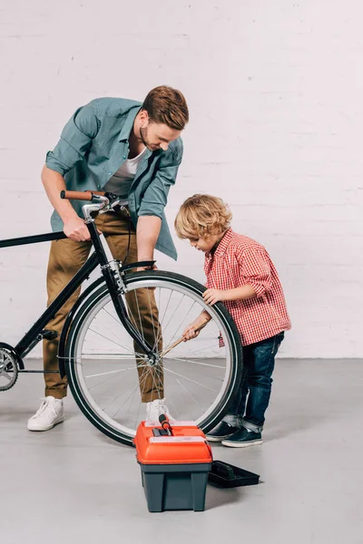 Selective focus of boy and his father repairing bicycle wheel in workshop — Stock Photo