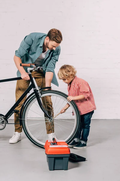 Messa a fuoco selettiva del ragazzo e suo padre riparazione ruota della bicicletta in officina — Foto stock