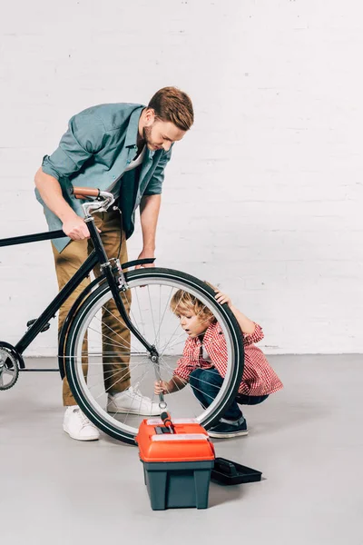 Kind und Vater reparieren Fahrradrad in der Nähe von Werkzeugkasten in Werkstatt — Stockfoto