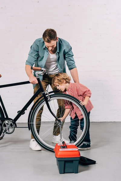 Menino e seu pai reparando roda de bicicleta na oficina — Fotografia de Stock