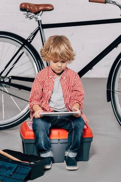 Lockiger kleiner Junge sitzt auf Werkzeugkiste und benutzt digitales Tablet — Stockfoto
