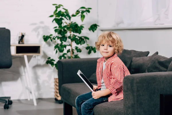 Niño alegre sentado en el sofá con la tableta digital - foto de stock