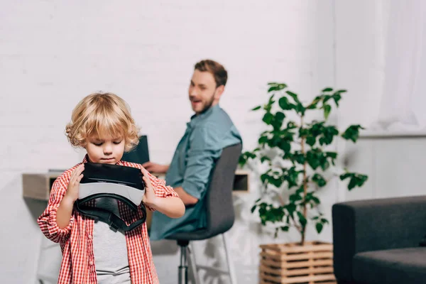 Selektiver Fokus des kleinen Kindes mit Virtual-Reality-Headset und seines Vaters, der zu Hause hinter ihm sitzt — Stockfoto