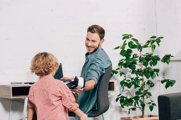 Ridendo uomo dando cuffia realtà virtuale al piccolo figlio — Foto stock