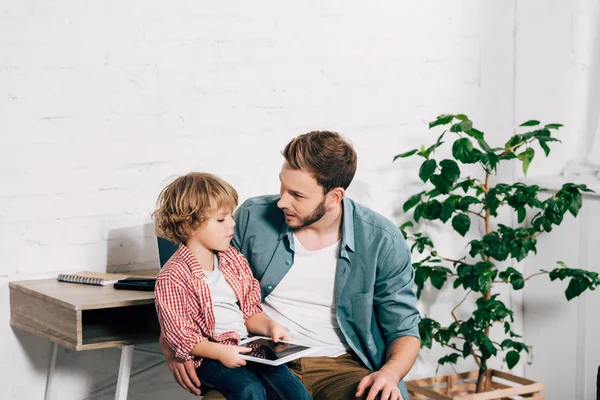 Selective focus of little kid holding digital tablet and sitting on father knees at home — Stock Photo