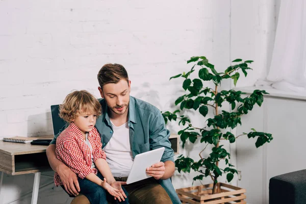 Vista de ángulo alto del hombre mostrando tableta digital a pequeño hijo en casa - foto de stock