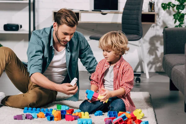 Lockenkopf und sein Vater spielen zu Hause mit bunten Plastikklötzen auf dem Boden — Stock Photo