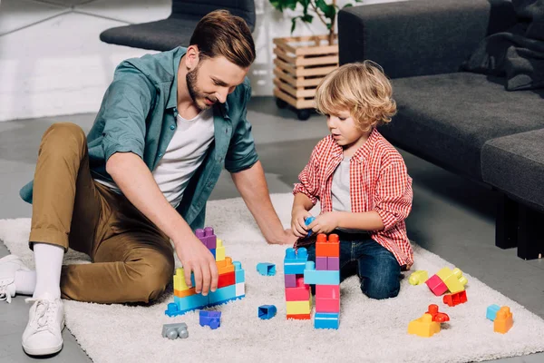 Мужчина с маленьким сыном играют дома с разноцветными пластиковыми блоками на полу — стоковое фото