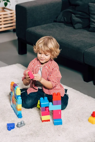 Menino encaracolado brincando com blocos de plástico coloridos no chão em casa — Fotografia de Stock