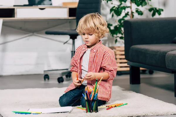 Lockige kleine Junge sitzt auf dem Boden mit bunten Filzstiften und weißem Papier zu Hause — Stockfoto