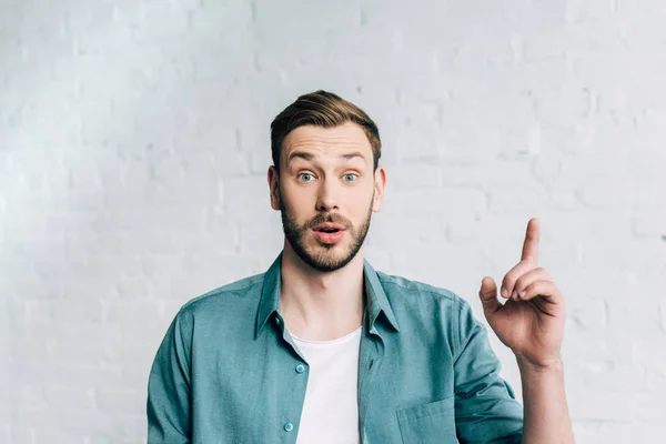 Emotional young man doing idea gesture in front of brick wall — Stock Photo