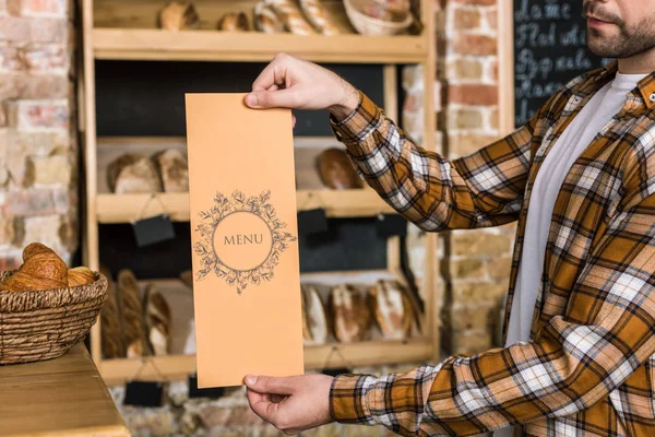 Male seller holding paper menu in hands at bakery — Stock Photo