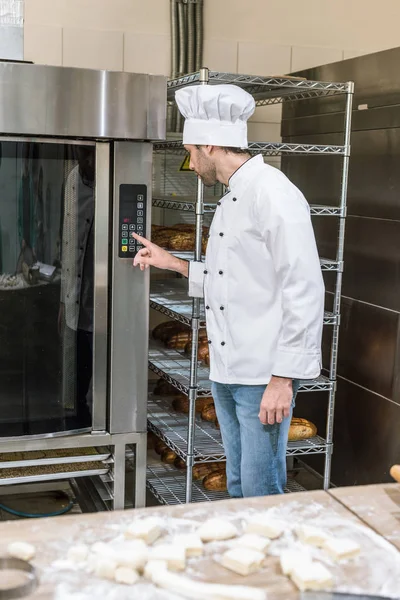 Мужчина пекарь нажав кнопку на духовке на кухне — стоковое фото