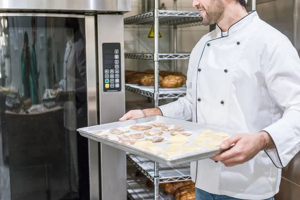 Vue recadrée du cuisinier mâle tenant la plaque de cuisson avec pâte crue près du four — Stock Photo