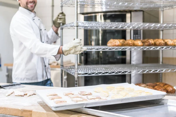 Souriant boulanger masculin en uniforme de chefs blancs travaillant à la cuisine — Photo de stock