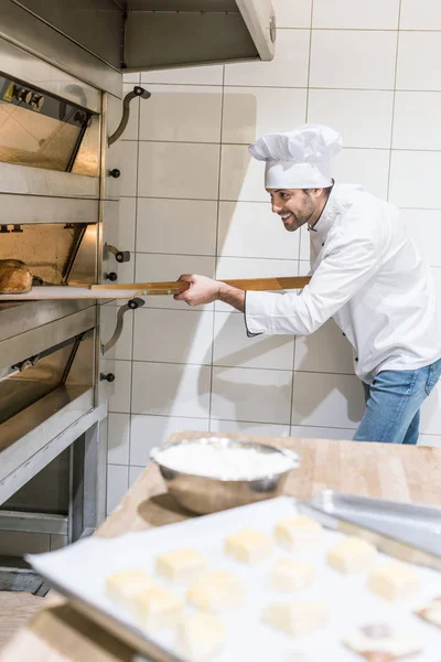Concentrated baker taking out hot bread from oven at kitchen — Stock Photo