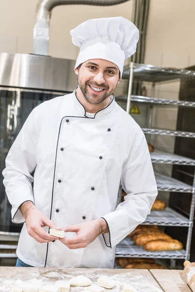 Padeiro alegre sorridente com produtos crus na cozinha — Fotografia de Stock