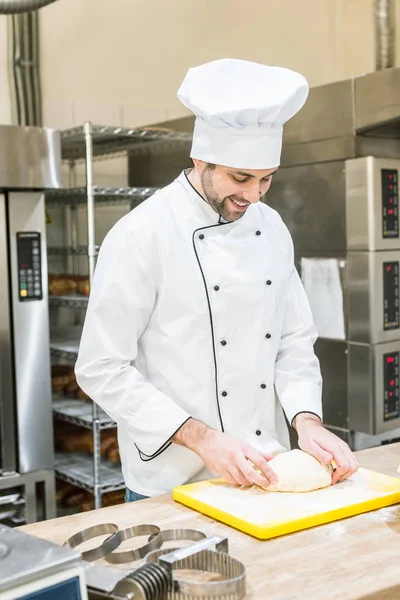 Sorrindo padeiro macho esmagar massa não cozida na cozinha — Fotografia de Stock