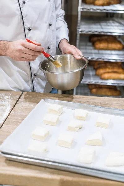 Primer plano de las manos de cocinero engrasar trozos de masa con cepillo de cocción - foto de stock