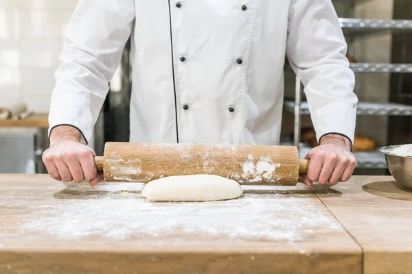 Close up of baker hands rolling out raw dough at wooden counter — Stock Photo