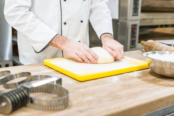 Primer plano de las manos del panadero con masa en la tabla de cortar - foto de stock