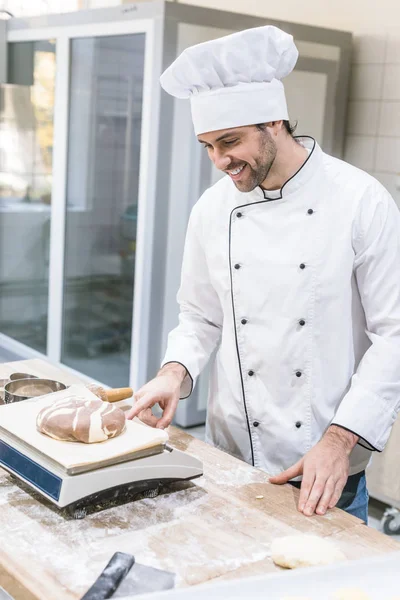 Panadero sonriente que pesa masa cruda en balanzas de cocina - foto de stock
