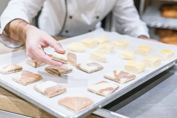 Vista ritagliata delle mani del fornaio con pasta cruda sul vassoio — Foto stock