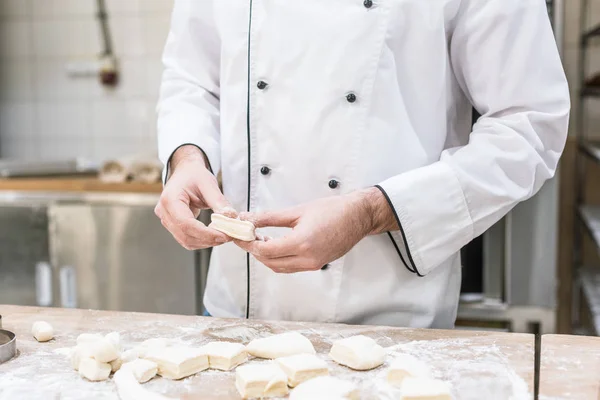 Cropped view of baker in chefs uniform cooking dough on wooden table — Stock Photo