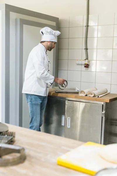 Chef de uniforme branco com utensílios de cozinha na cozinha da padaria — Fotografia de Stock